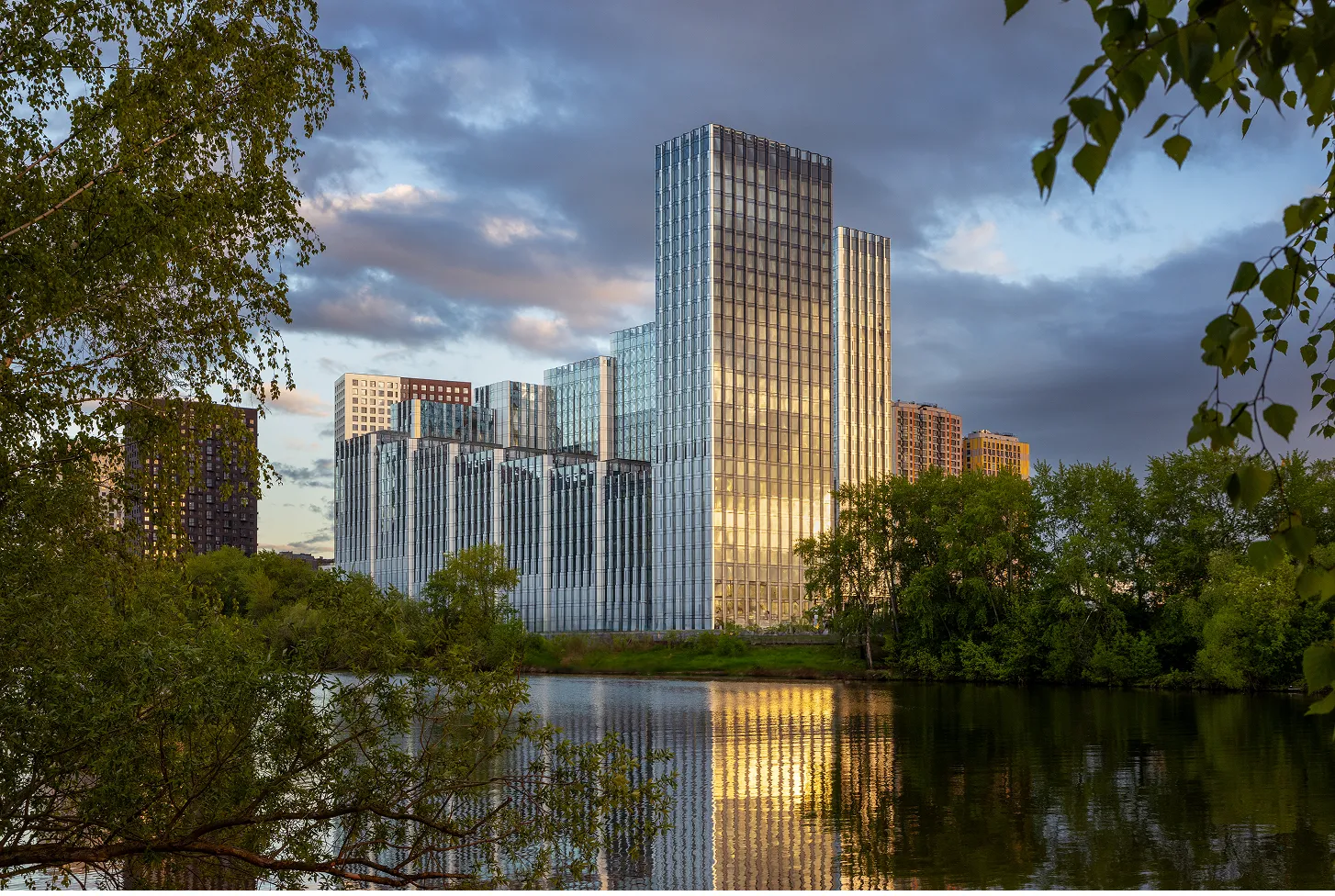ЖК Береговой словно вырастает из самой реки — его волнообразные фасады мерцают в воде, а зелень парка обнимает современную архитектуру